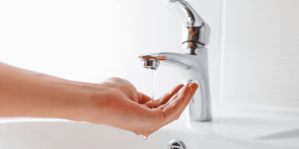 Main sous un robinet avec un faible filet d’eau, illustrant un problème de pression d’eau au domicile.